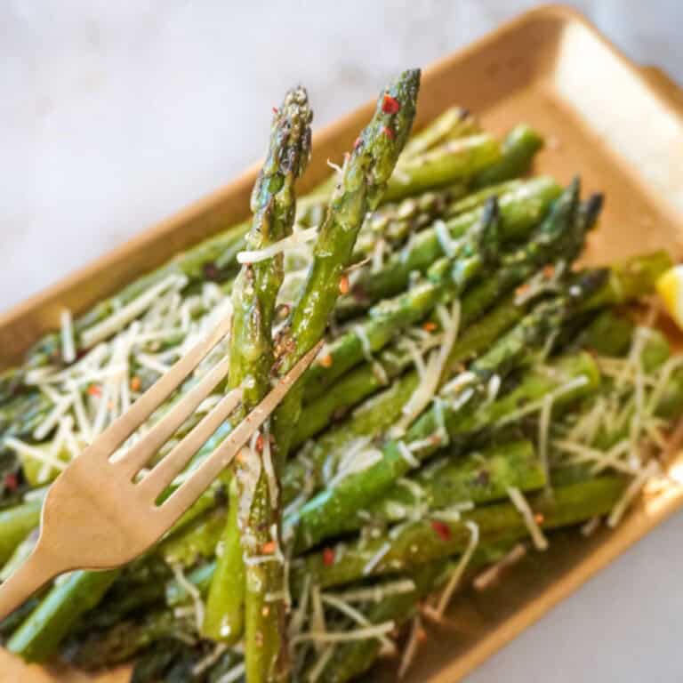 A close-up of a fork holding two spears of pan-fried asparagus with melted Parmesan and red pepper flakes.